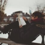 Chica leyendo un libro de romance en una banca del parque en invierno