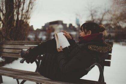 Chica leyendo un libro de romance en una banca del parque en invierno