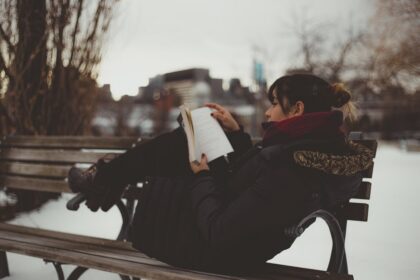 Chica leyendo un libro de romance en una banca del parque en invierno