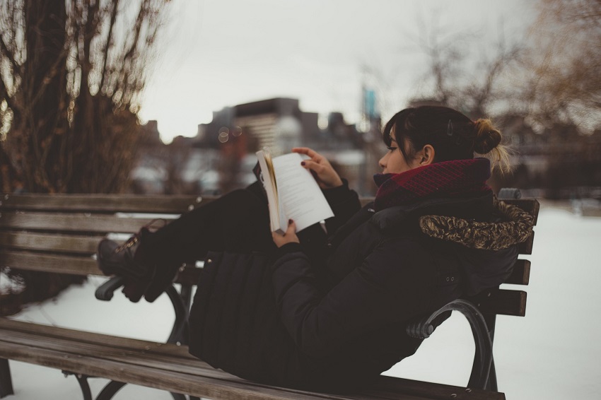 Chica leyendo un libro de romance en una banca del parque en invierno